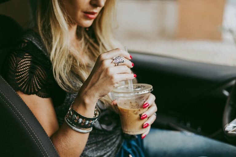 Close-up of a woman holding a plastic cup of iced coffee inside a car with stylish accessories.