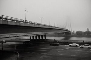 A misty morning view of a city bridge with light traffic and pedestrians, captured in black and white.