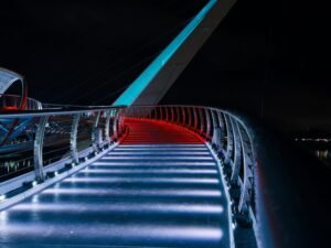 Curved modern bridge illuminated with vibrant red and blue lights at night.