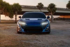 A sleek blue sports car parked under a bridge surrounded by palm trees during sunset.