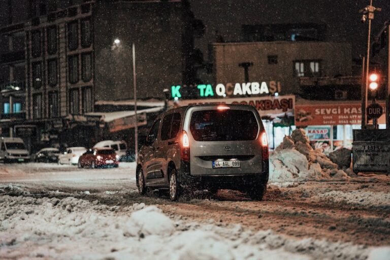 A car navigating snowy city streets at night during winter.