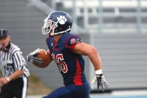 Focused American football player running with the ball during a game outdoor.