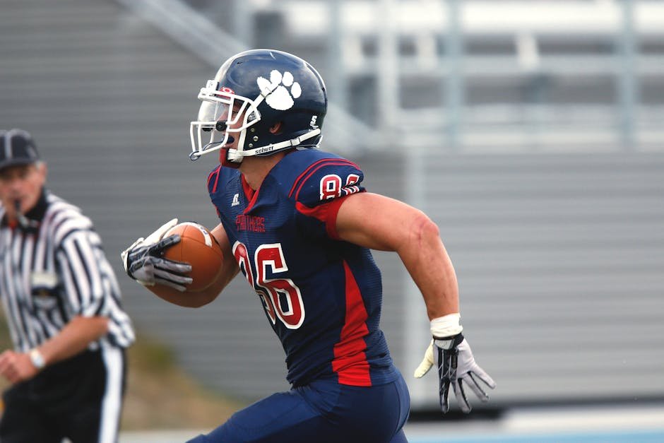 Focused American football player running with the ball during a game outdoor.