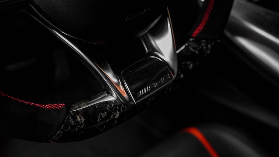 Close-up of a luxury car steering wheel with detailed red stitching and chrome accents.