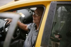 Middle-aged taxi driver inside yellow cab, focused on driving.