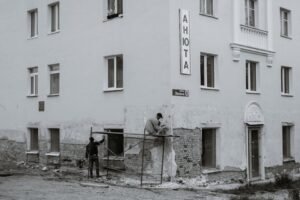 Two workers renovating an urban residential building exterior in black and white.