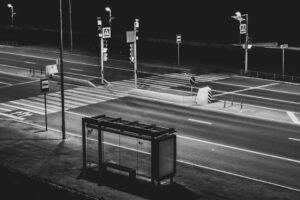 Black and white image of an empty city crosswalk and bus stop at night.