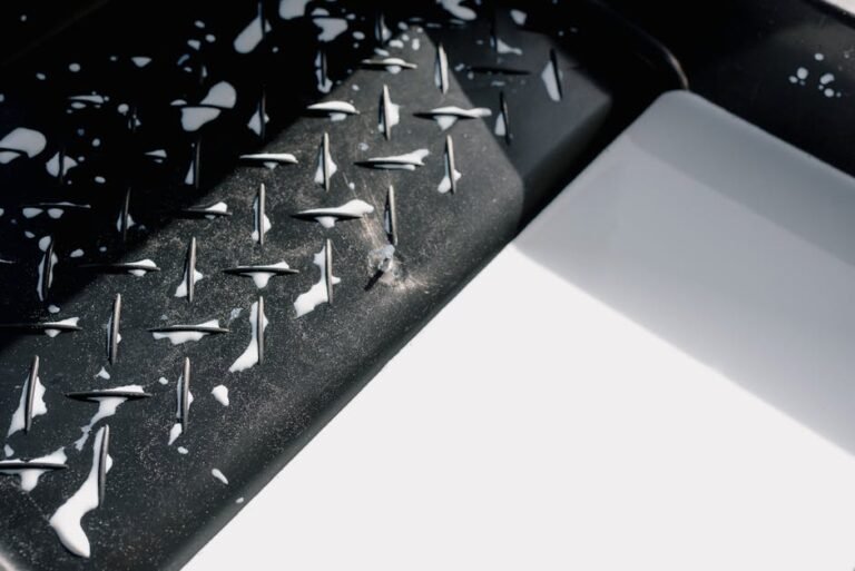 Close-up of paint drips on textured black metal with white background.